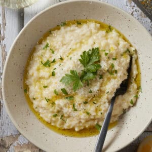 Easy oven-baked risotto in a bowl with parsley lemon and olive oil garnishes.