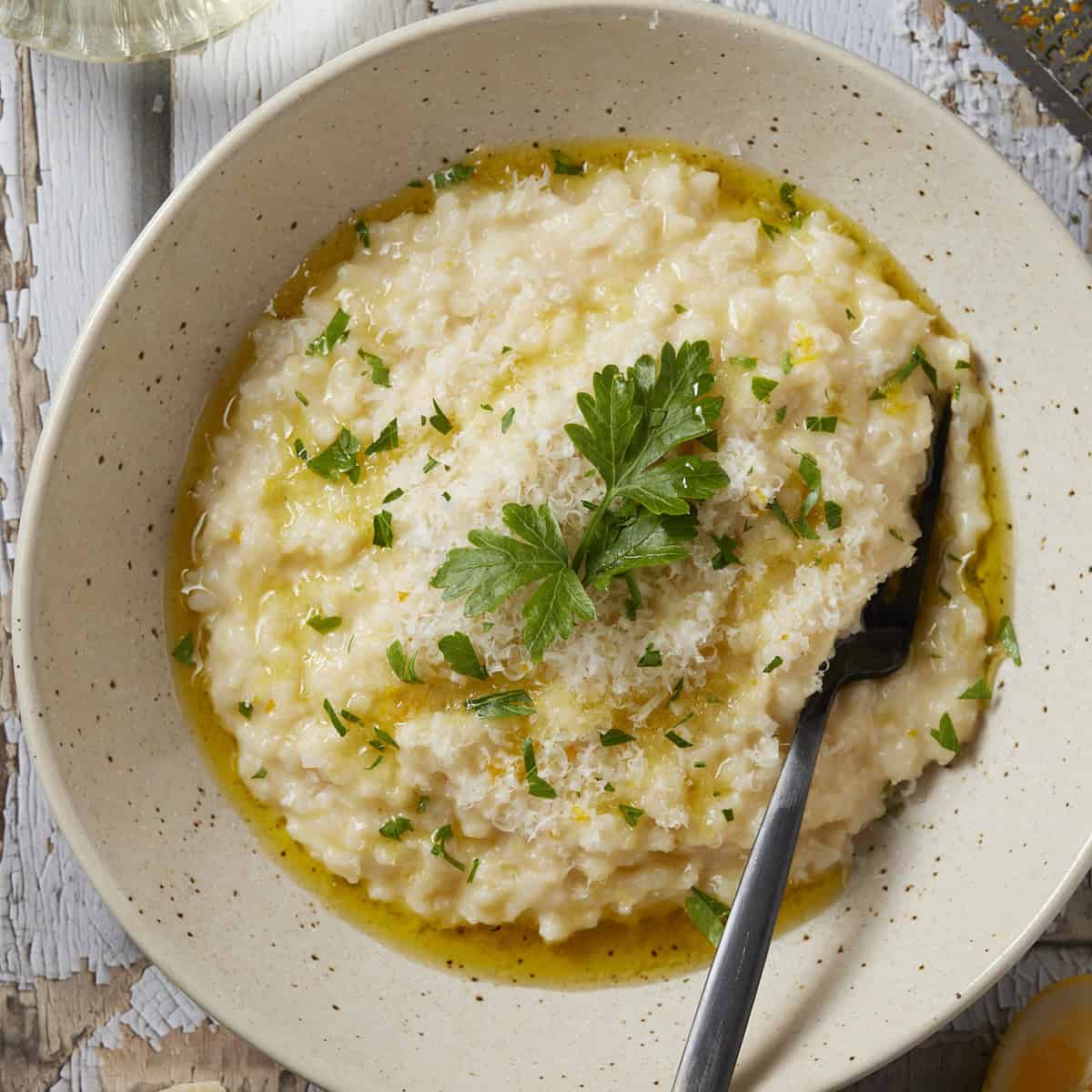 Easy oven-baked risotto in a bowl with parsley lemon and olive oil garnishes.