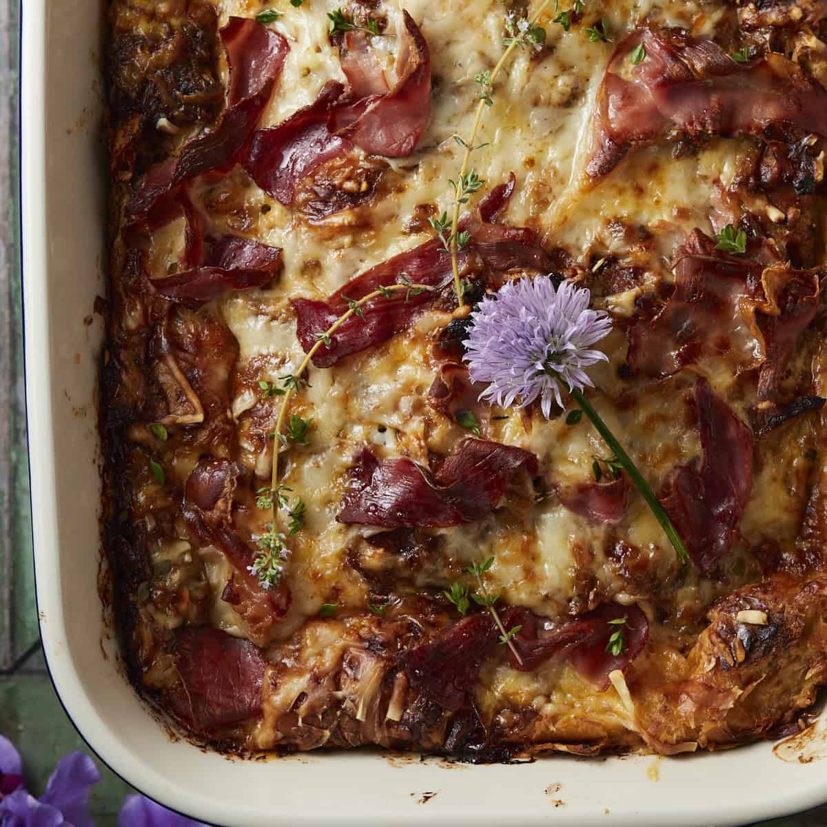 French onion croissant bake in a baking dish with herbs on top.
