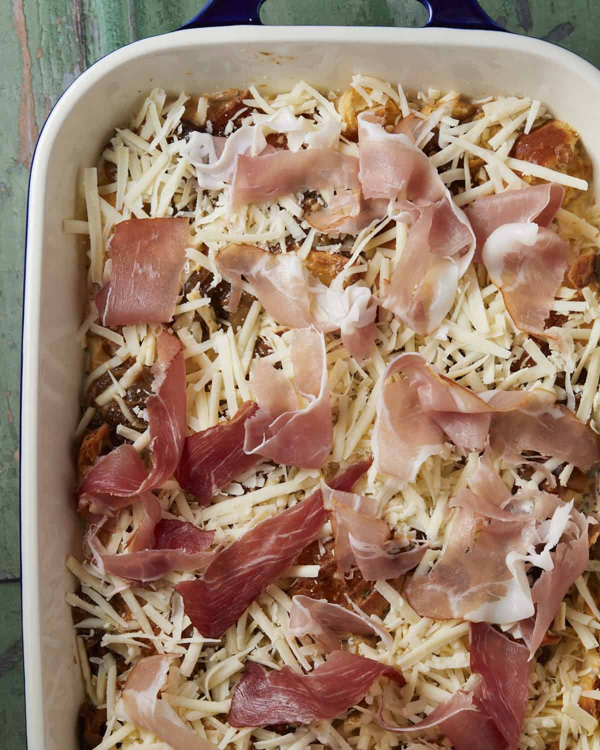 Adding cheese and prosciutto to the baking dish before baking. 