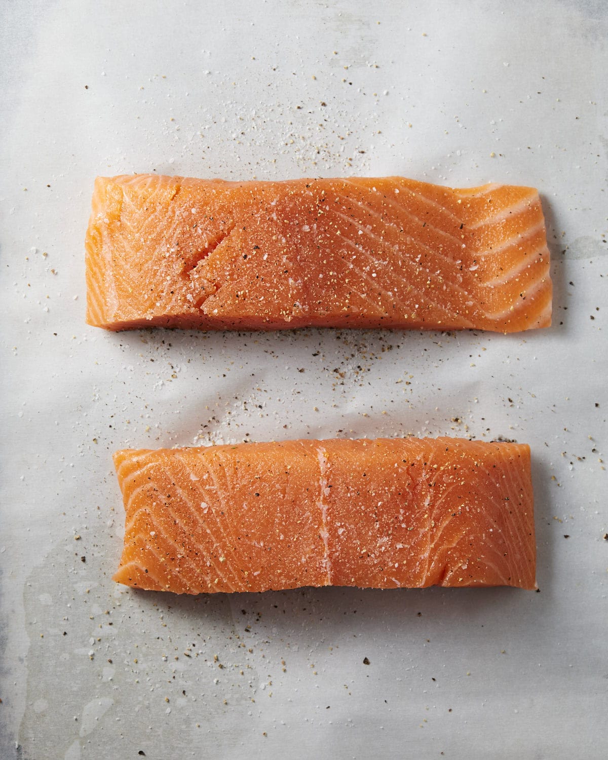 Salmon filets prepped with salt and pepper on a rimmed baking sheet lined with parchment paper.
