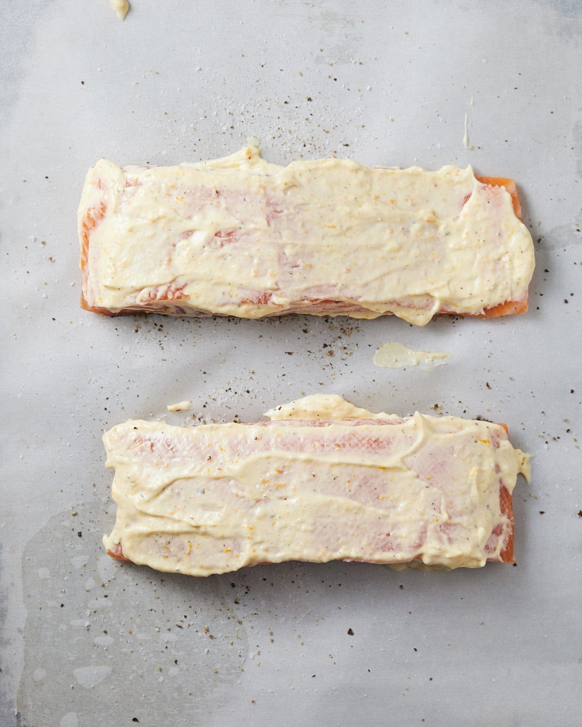 Salmon filets topped with mayo sauce on baking sheet. 