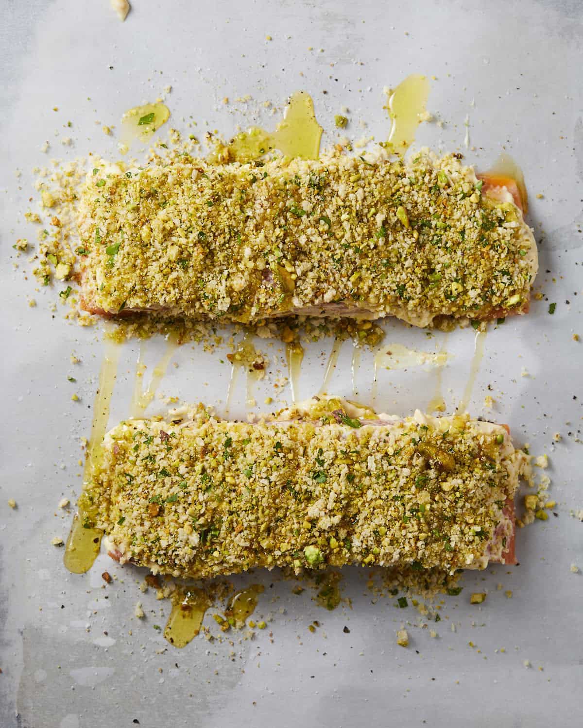 Salmon filets with pistachio crust and olive oil drizzle on baking sheet. 