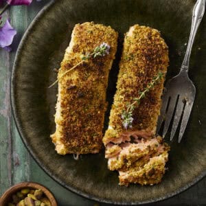 Pistachio crusted salmon on a green plate and serve with fresh flowering thyme.