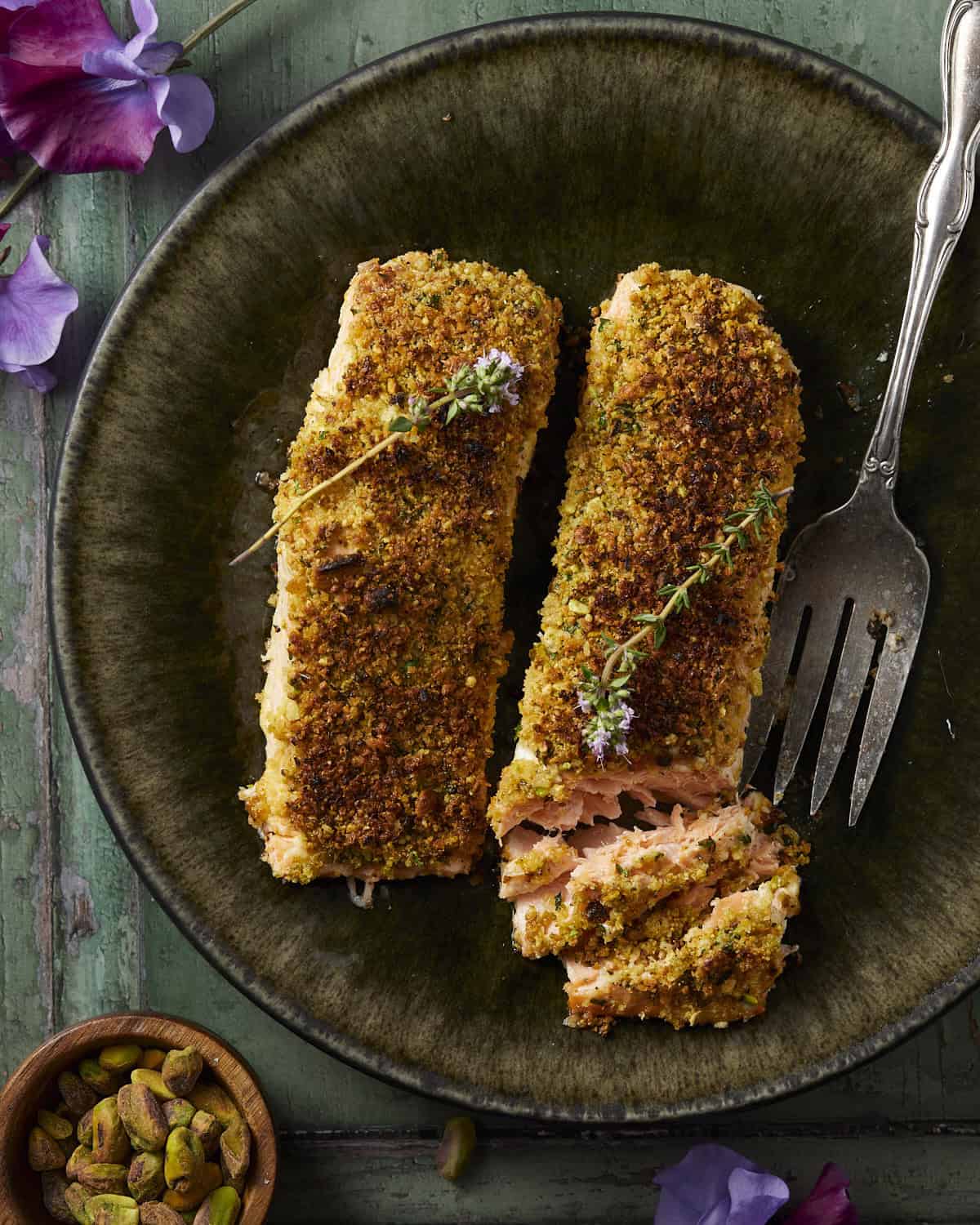 A green plate with 2 pieces of salmon baked with a pistachio crust. 