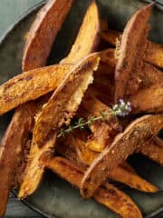 Sweet potato wedges crusted in parmesan cheese on a plate with fresh thyme.