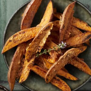 Sweet potato wedges crusted in parmesan cheese on a plate with fresh thyme.