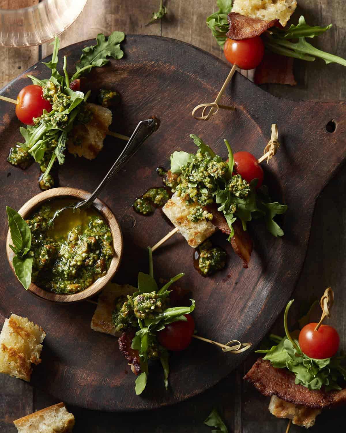 Blt skewers served with pistachio basil pesto dressing on a wooden plate. 