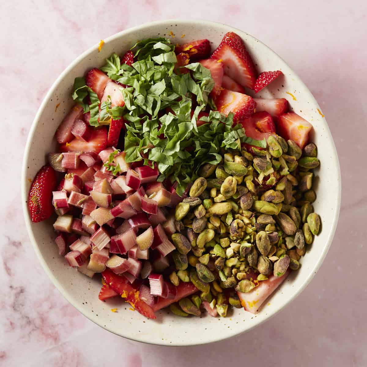 Cut strawberries, basil and pistachios with rhubarb in a bowl.