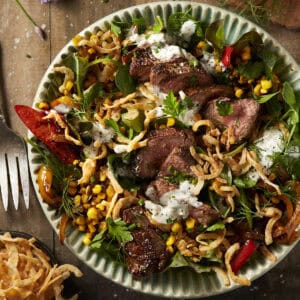 A blue bowl filled with steak salad with fried onions and blue cheese dressing.