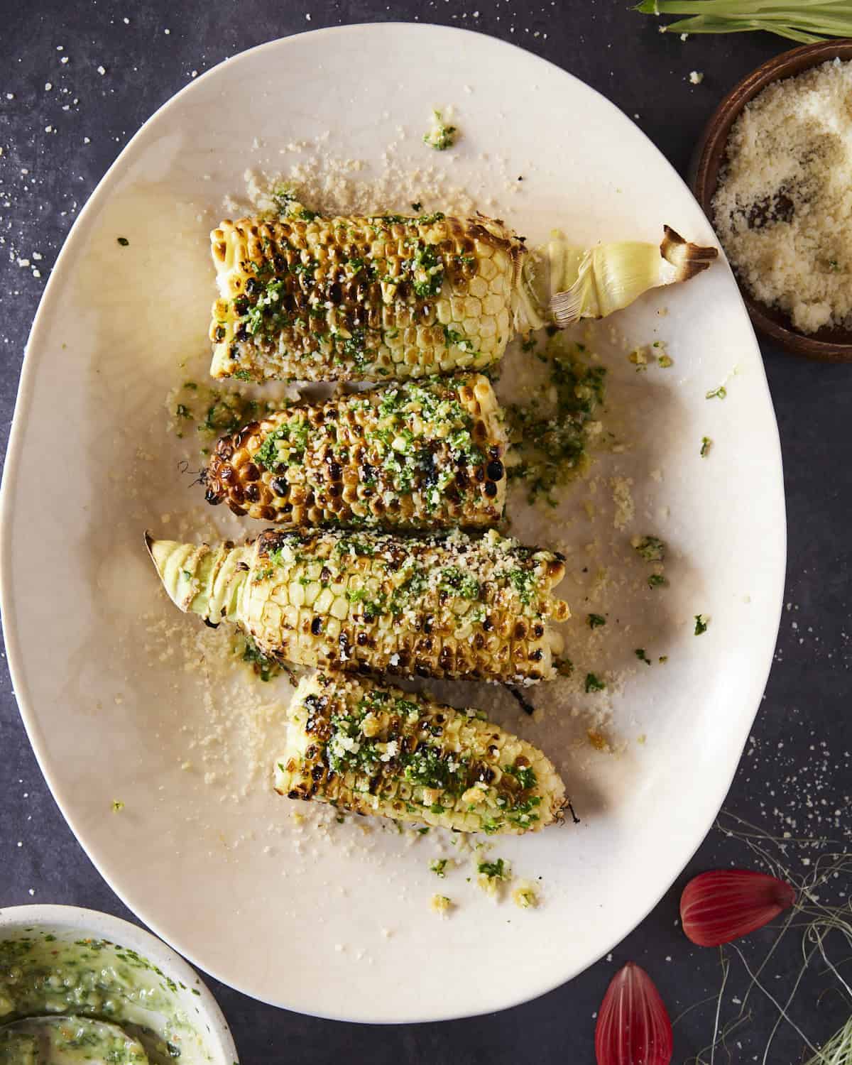 A plate full of grilled corn brushed with chimichurri and sprinkled with cheese.