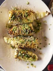 A plate of grilled corn with a chimichurri butter sauce.
