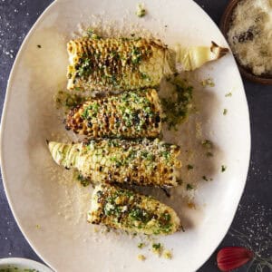A plate of grilled corn with a chimichurri butter sauce.
