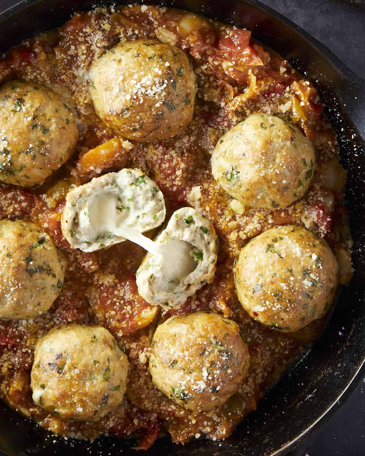Up close image of meatballs stuffed with melty cheese on tomato sauce.