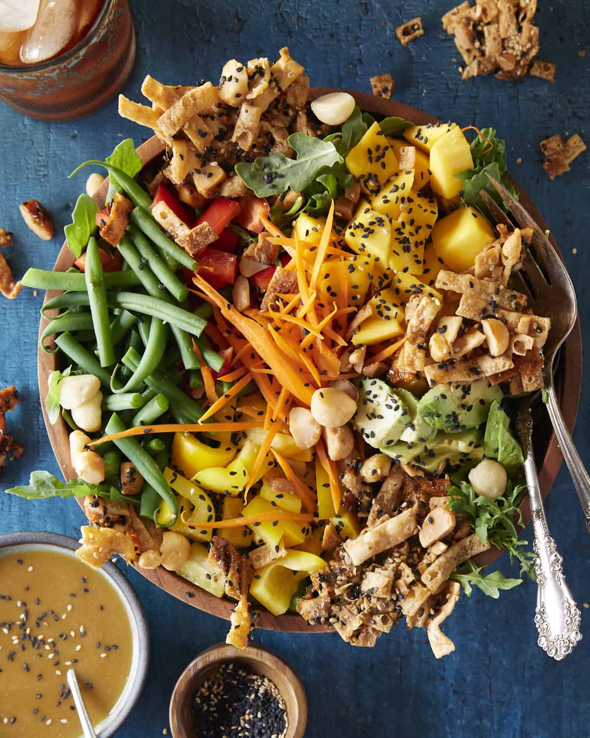 A luau style salad in a wooden bowl with a blue background. 