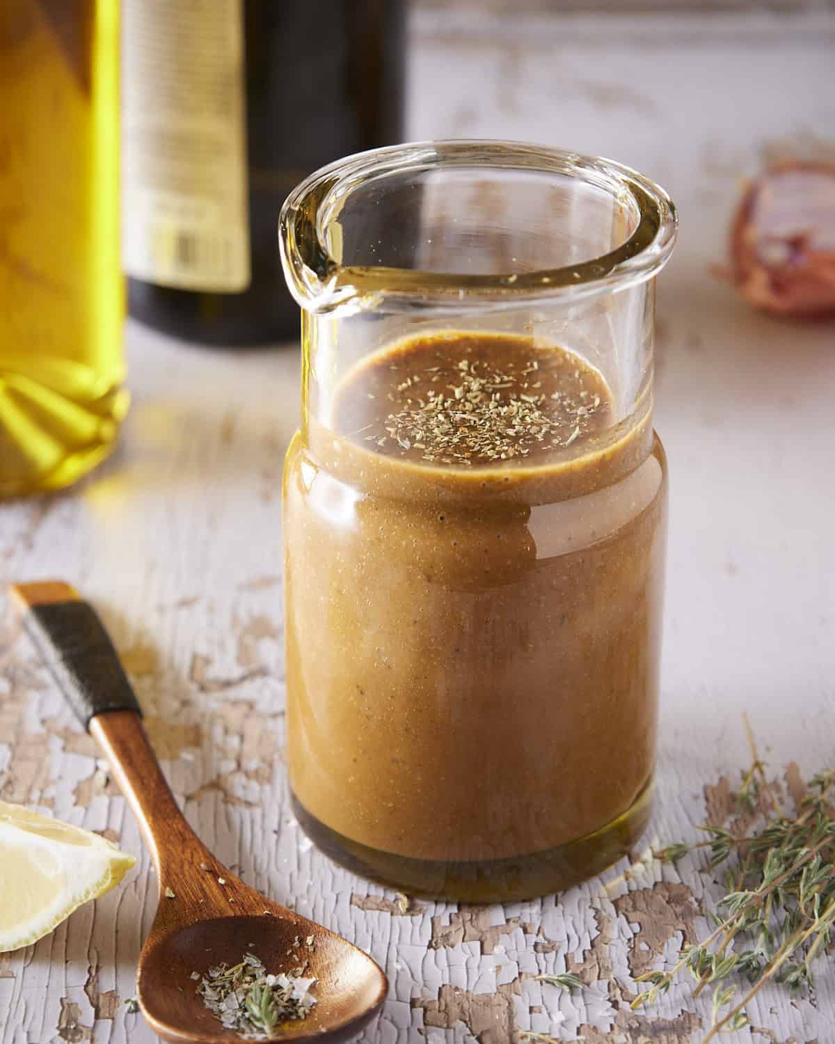 Homemade balsamic vinaigrette in glass dressing jar with a spoon and lemon wedge on the side. 