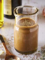 Homemade balsamic vinaigrette in glass dressing jar with a spoon and lemon wedge on the side.