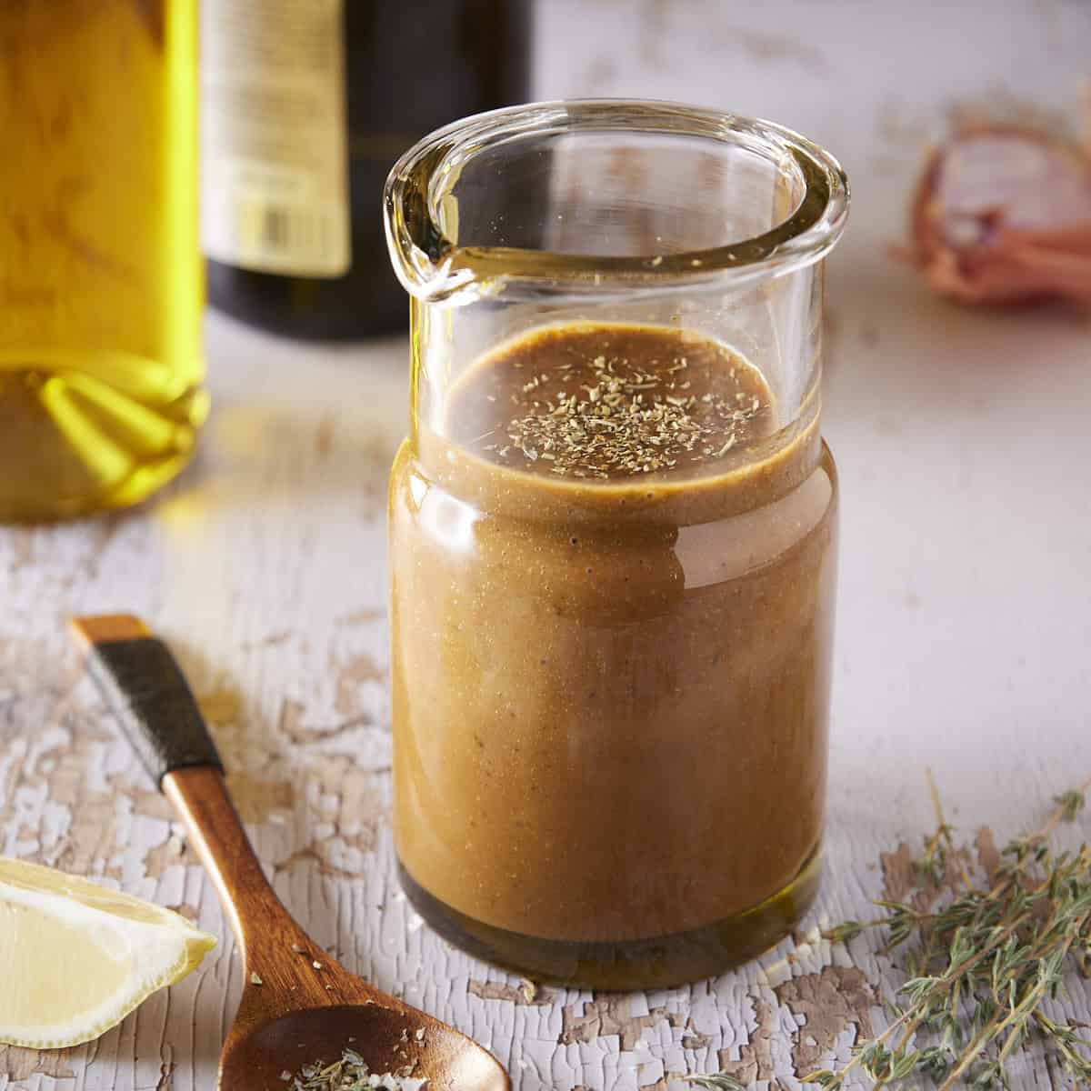 Homemade balsamic vinaigrette in glass dressing jar with a spoon and lemon wedge on the side.