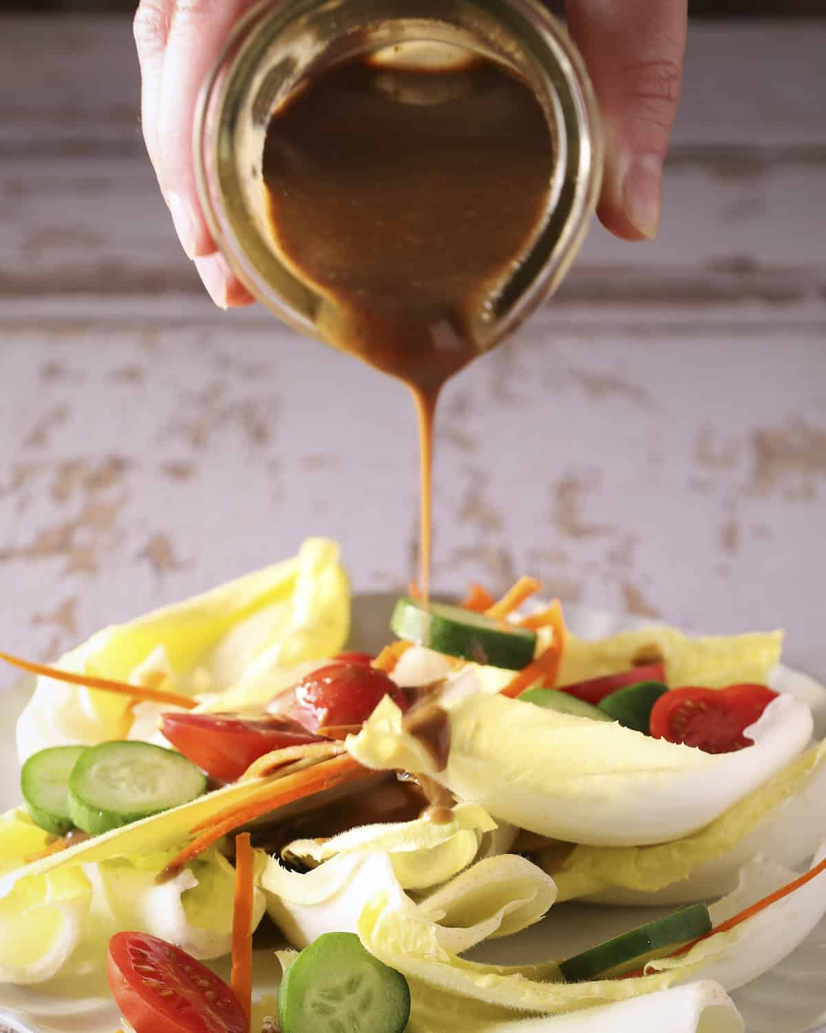 Balsamic dressing being drizzled over a salad with cucumbers and tomatoes.