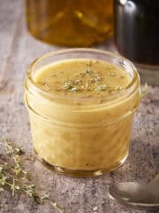 Homemade maple vinaigrette in a mason jar. Spoon and fresh thyme on the side.