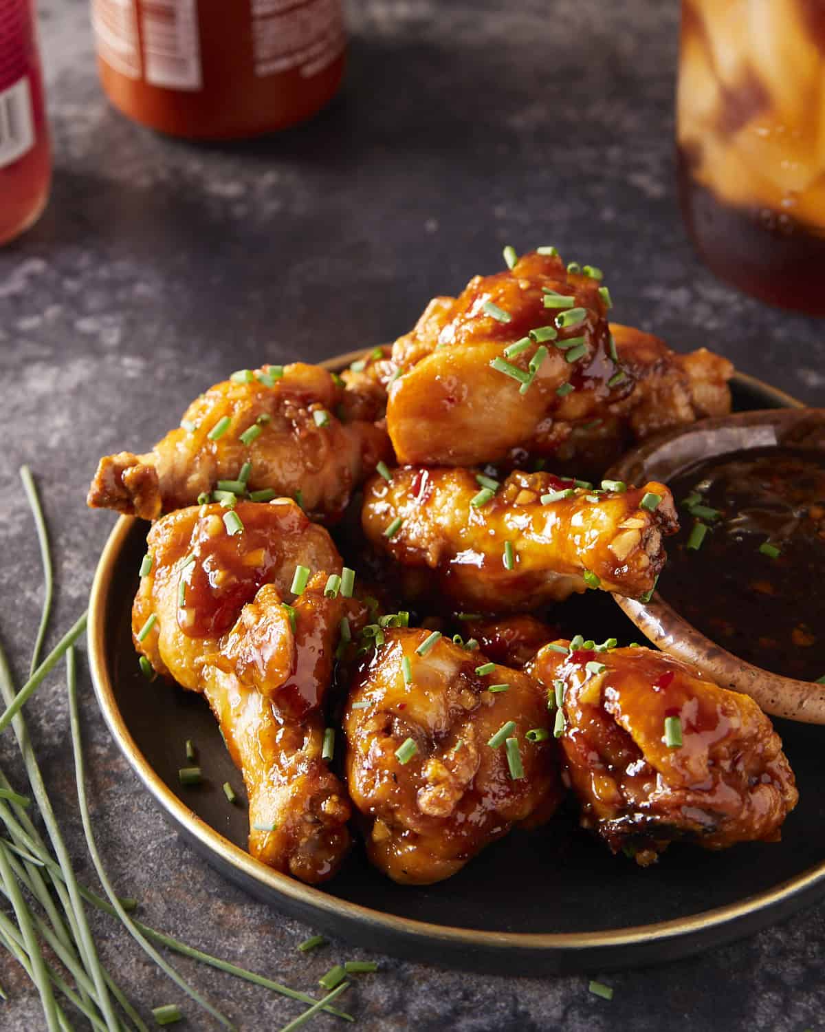 Sticky-sweet chili wings with sauce on the side sprinkled with chives.