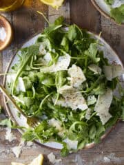 Overhead shot of a simple arugula salad on a rustic plate with a rustic wooden background.