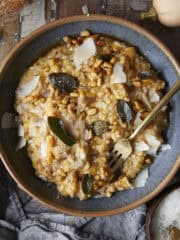 Butternut squash risotto in a bowl with fork topped with crispy sage, pine nuts and parmesan cheese.
