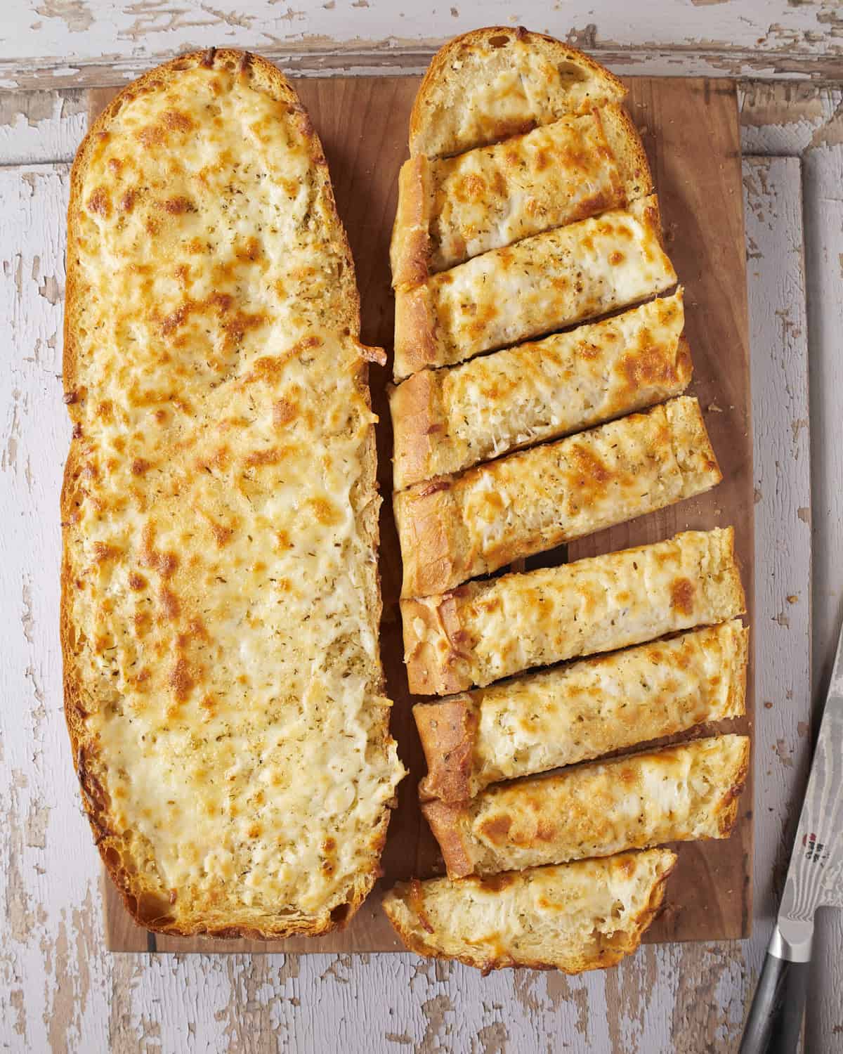 A loaf of cheesy garlic bread on half sliced and not the other.