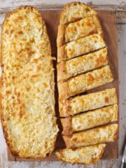 Cheesy garlic bread half cut on a cutting board.