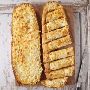 Cheesy garlic bread half cut on a cutting board.