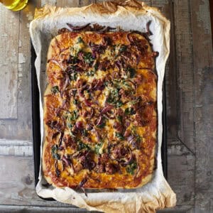 A baked sheet pan pizza with rustic parchment paper sliced with sausage, onions and chard.
