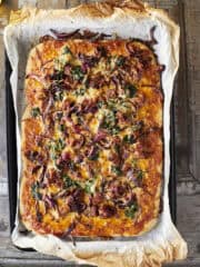 baked sheet pan pizza with rustic parchment paper sliced with sausage, onions and chard.
