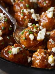 Buffalo chicken meatballs in a skillet with one in a spoon topped with blue cheese and chives.