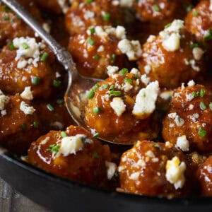 Buffalo chicken meatballs in a skillet with one in a spoon topped with blue cheese and chives.