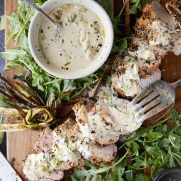 Pork tenderloin cut on a cutting board with sauce and arugula.
