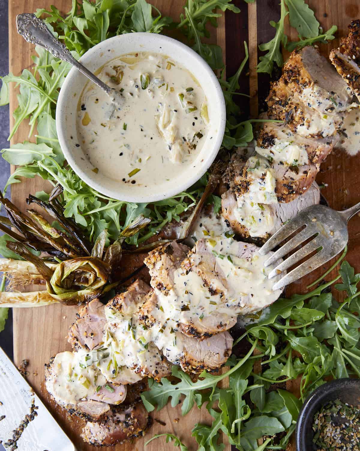 Pork tenderloin cut on a cutting board with sauce and arugula.