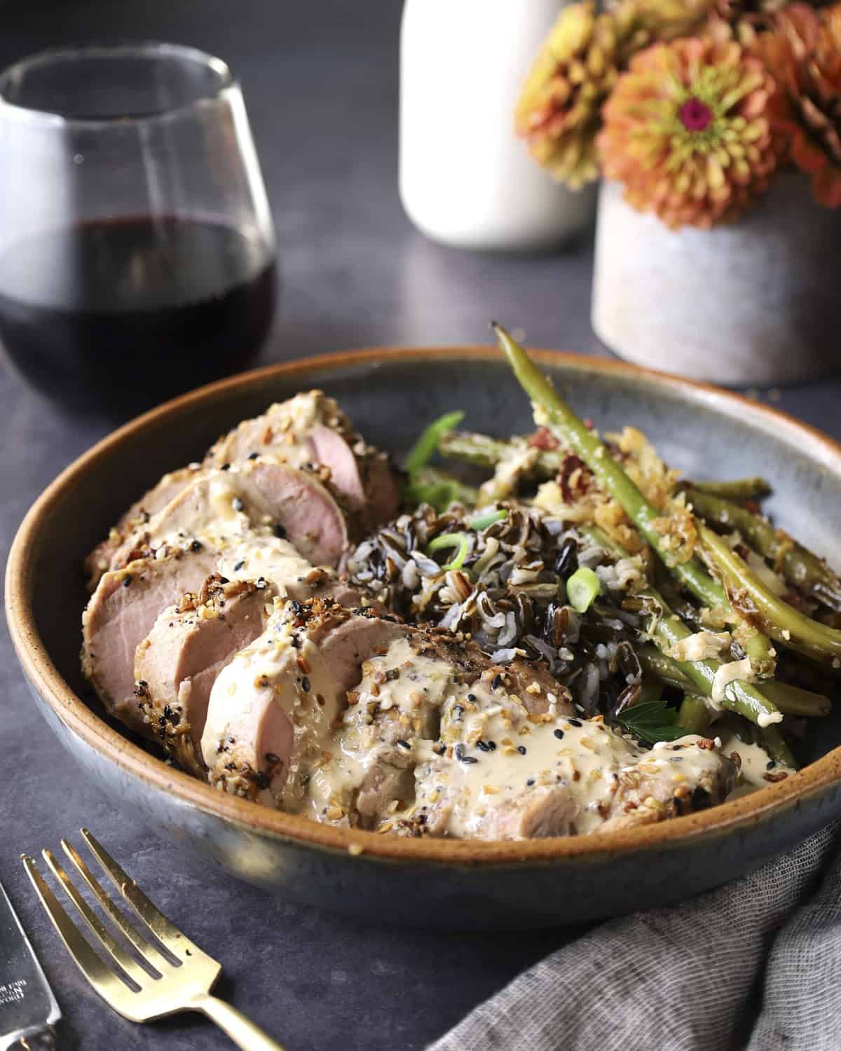 A black bowl filled with sliced pork tenderloin, wild rice and green beans with a side view.