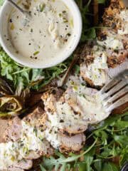 Crusted pork tenderloin with everything spice sliced on a cutting board with a cream cheese sauce.