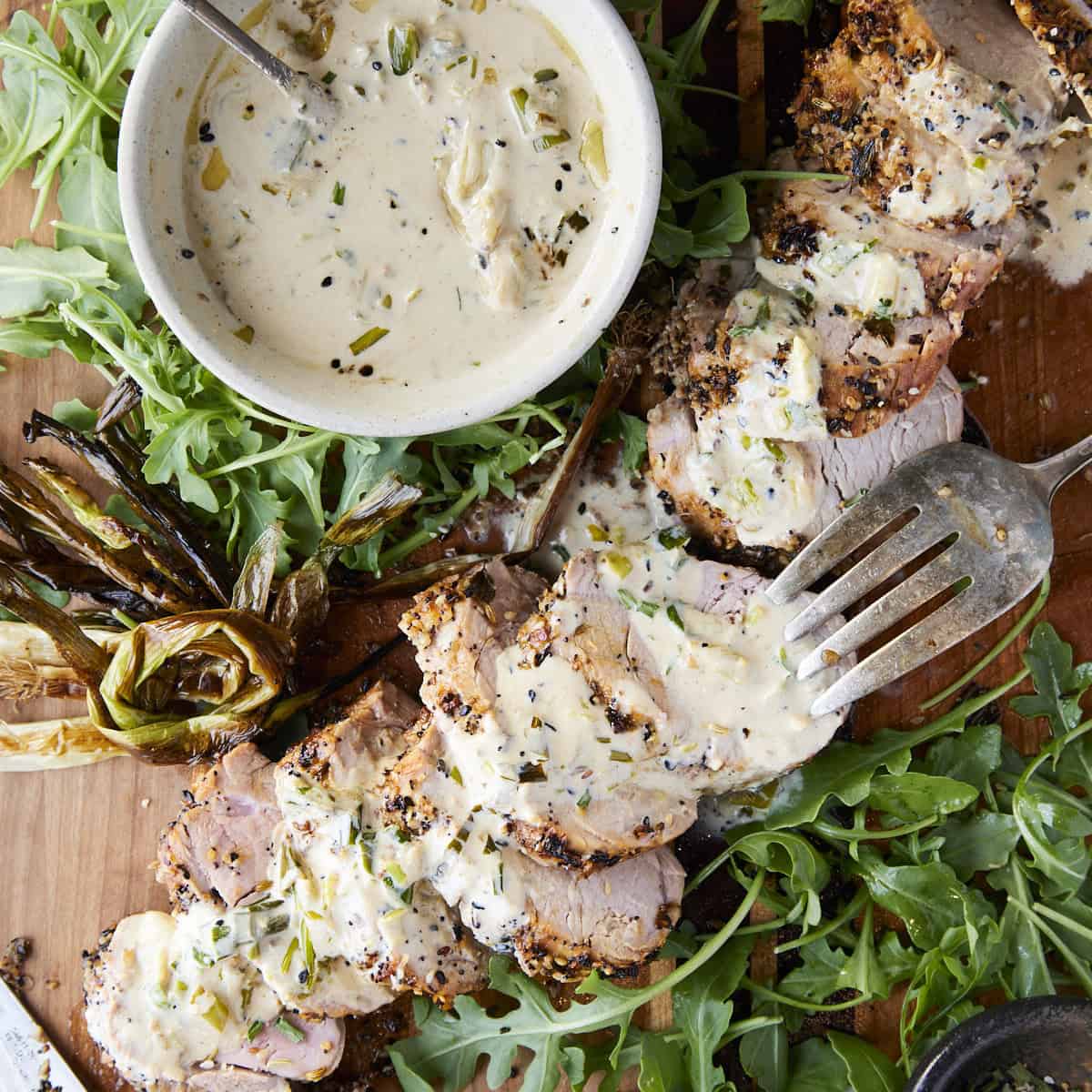Crusted pork tenderloin with everything spice sliced on a cutting board with a cream cheese sauce.