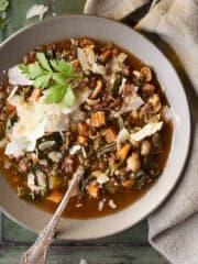 Lentil soup in a bowl with a spoon topped with shaved parmesan and parsley.