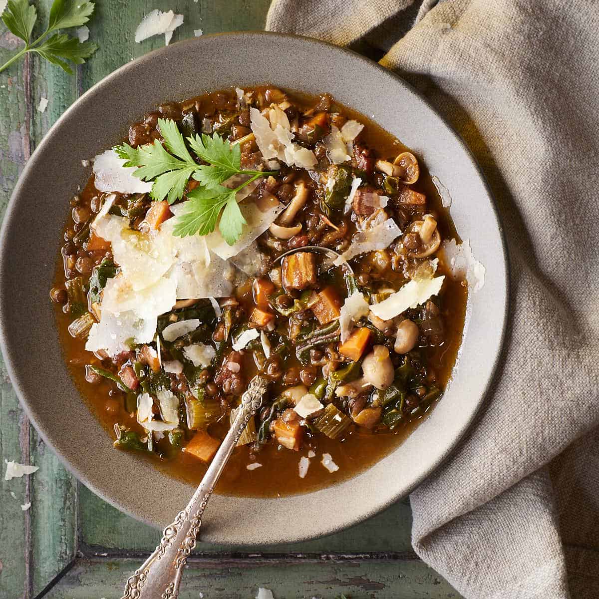 Lentil soup in a bowl with a spoon topped with shaved parmesan and parsley.