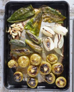 A sheet pan filled with charred vegetables for chile verde.