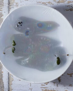 Steaming the charred poblano peppers in a bowl with plastic wrap.
