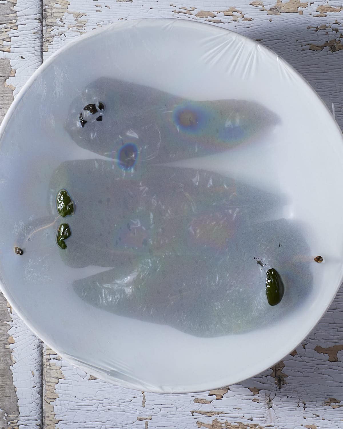 Steaming the charred poblano peppers in a bowl with plastic wrap.