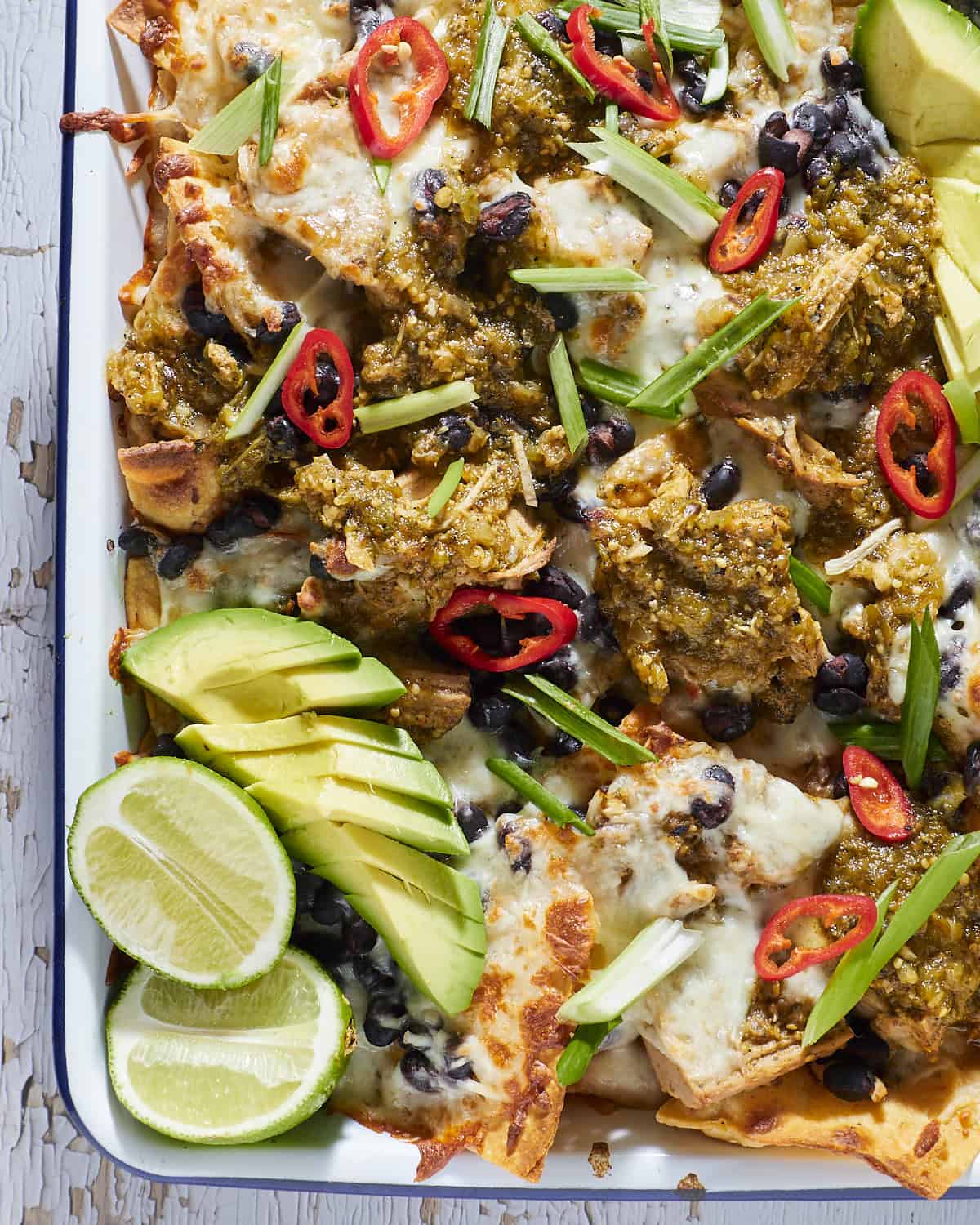 Nachos on a sheet pan with avocado and lime.