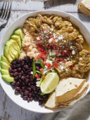 Chile verde in a bowl with beans, rice, avocado and garnishes.
