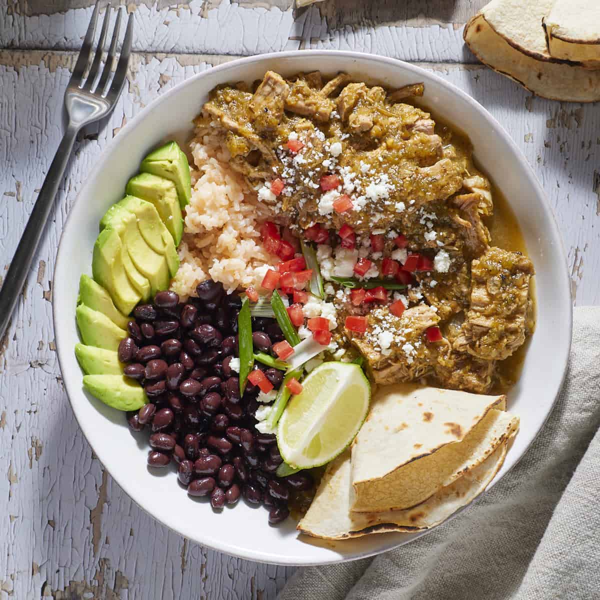 Chile verde in a bowl with beans, rice, avocado and garnishes.